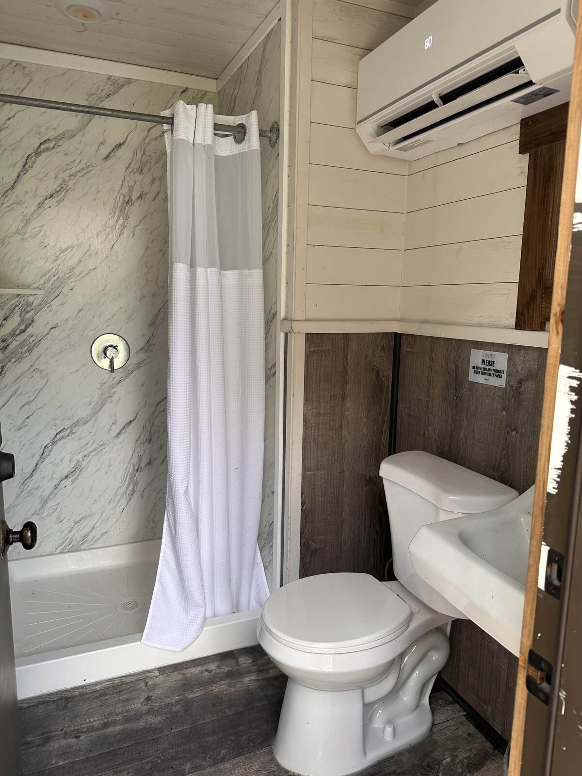 Inside a private glamping tent bathroom with a full shower and wall-mounted air conditioning at Peace River Oaks, Bowling Green, Florida